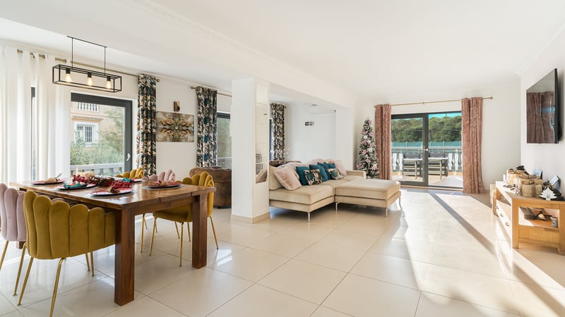 Espace de vie lumineux avec chaises en velours moutarde, canapé beige et grandes baies vitrées ouvrant sur une terrasse.