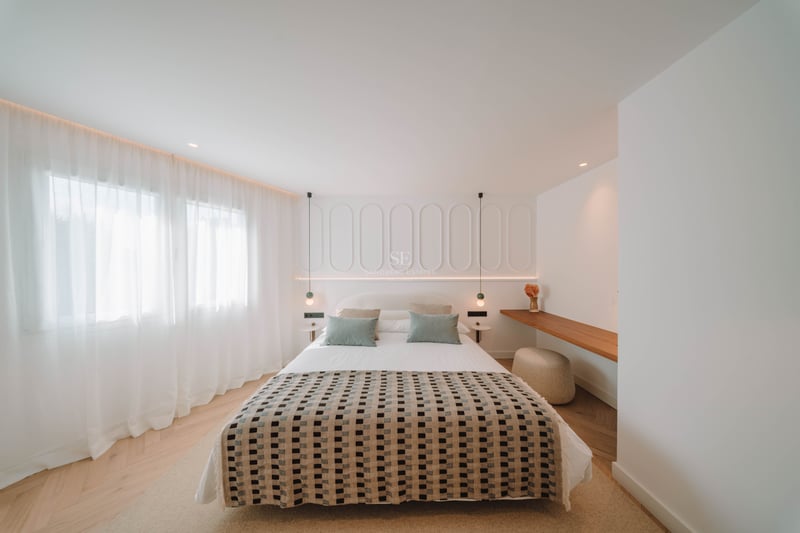 Chambre moderne lumineuse avec couvre-lit à motifs, mur de tête de lit à panneaux blancs et parquet en chevrons.