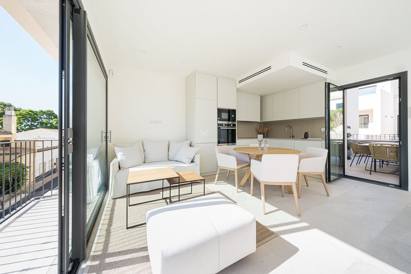 Bright open-plan living and dining area with minimalist kitchen and glass doors opening to a sunny balcony.