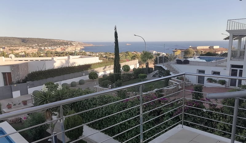 Vue surélevée depuis une terrasse avec garde-corps en acier sur la Méditerranée et les collines côtières.