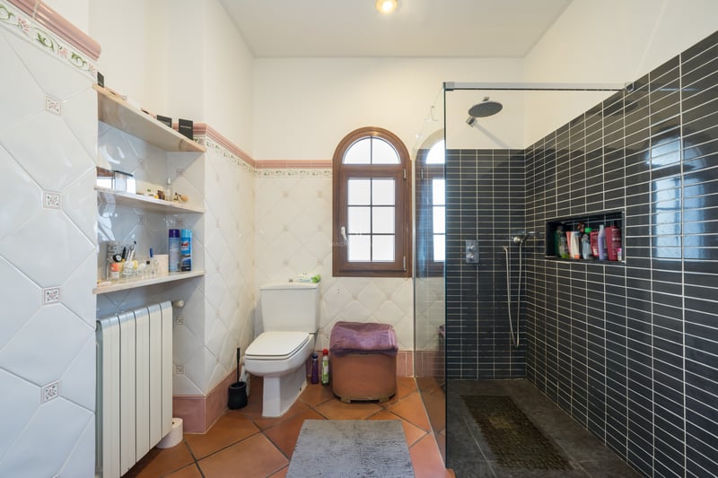 Bathroom featuring terracotta floors, decorative wall tiles, an arched wooden window, and a modern glass walk-in shower.