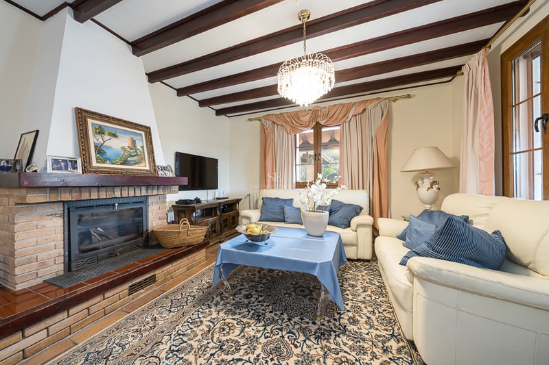Salon avec cheminée en briques, poutres apparentes, canapés en cuir crème et lustre en cristal.