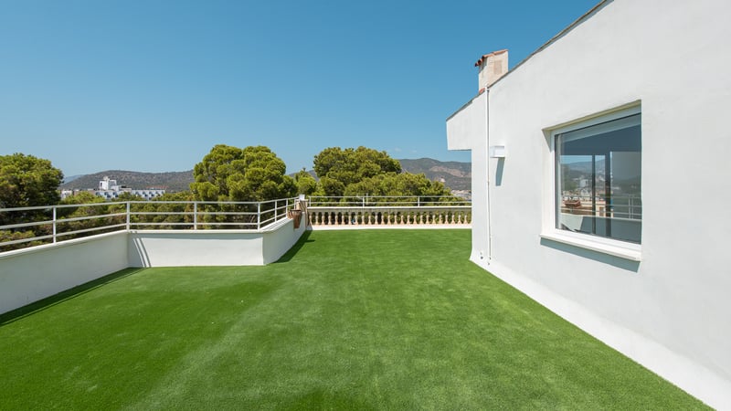 Grande terrasse sur le toit avec gazon synthétique, garde-corps en métal et vue sur les collines.