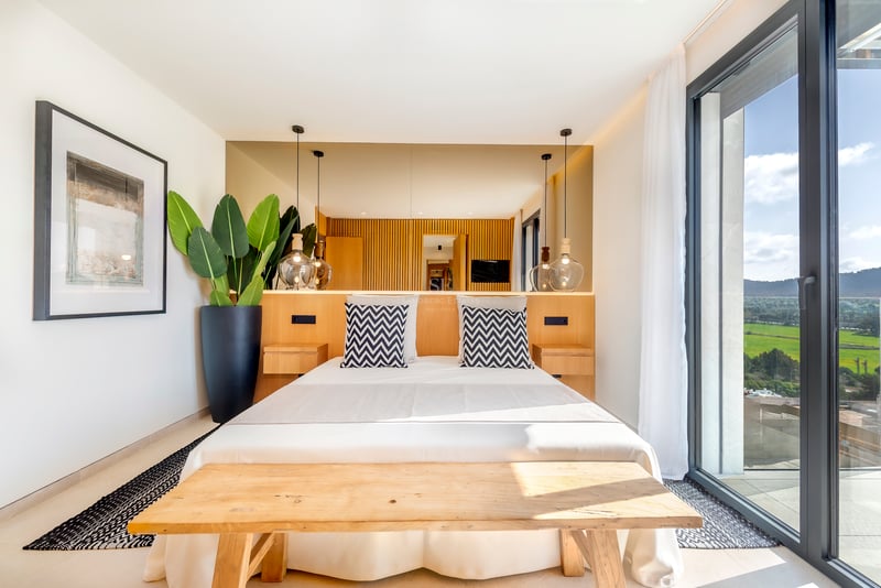 Chambre contemporaine lumineuse avec tête de lit en bois, suspensions en verre et baies vitrées ouvrant sur la nature.