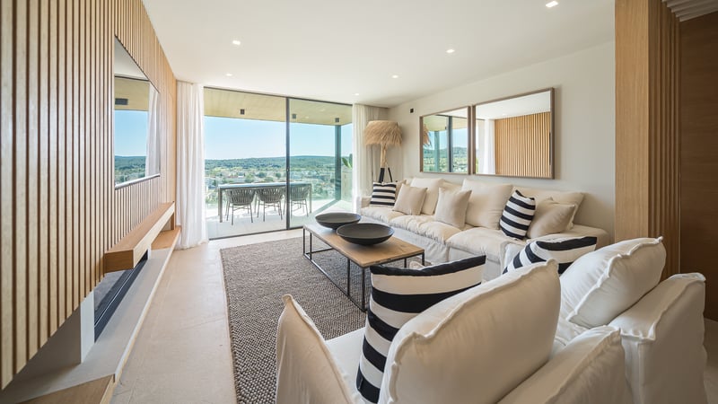 Salon moderne avec canapé blanc, mur en lattes de bois et baies vitrées s'ouvrant sur une terrasse.