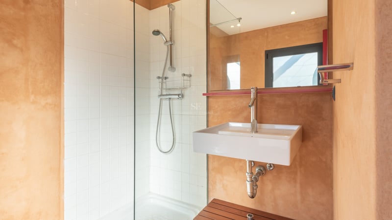 Modernt badrum med duschvägg i glas, vita kakelplattor och varma terracotta-färgade väggar med ett vitt tvättställ.