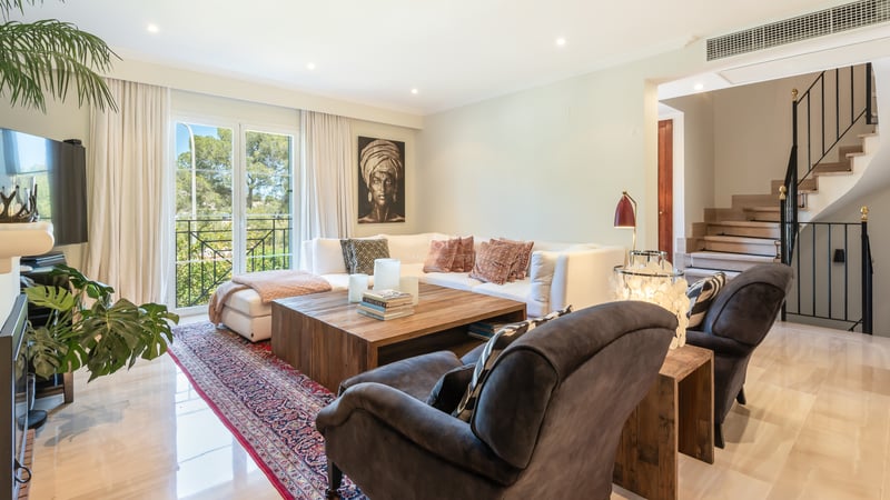 Sophisticated living room featuring a white sectional sofa, rustic wood table, marble floors, and garden views.