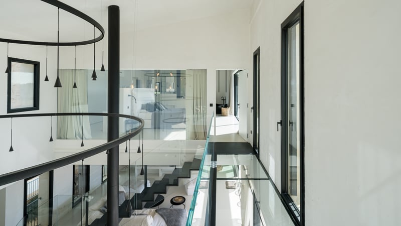 Modern hall med gångbro i glas, svart trappa och stora fönsterpartier i en lyxig villa.