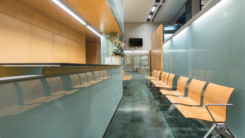 Espace de réception moderne avec cloisons en verre dépoli, sièges en bois clair et sol en marbre vert foncé.