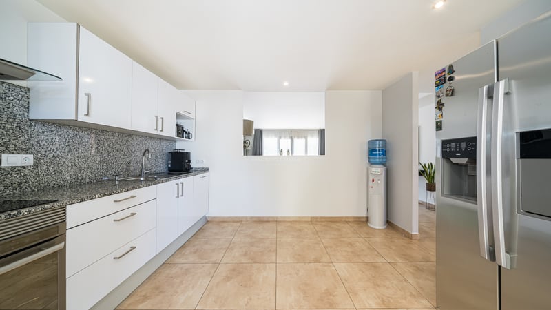 Ett modernt kök med vita skåp, spräckliga bänkskivor i granit och ett stort kylskåp i rostfritt stål.