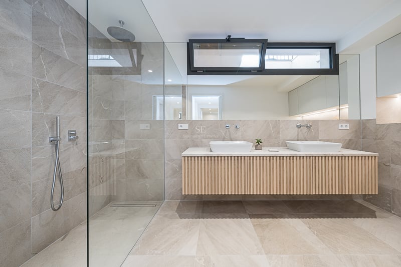 Modern bathroom featuring a walk-in glass shower, sand-colored stone tiles, and a floating wood double vanity.