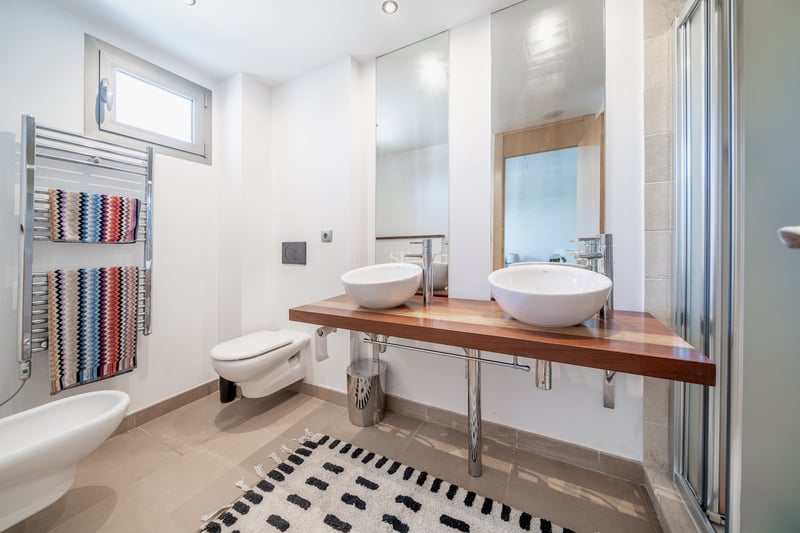 Salle de bain lumineuse avec plan de toilette en bois, deux vasques blanches, sèche-serviettes et grands miroirs.