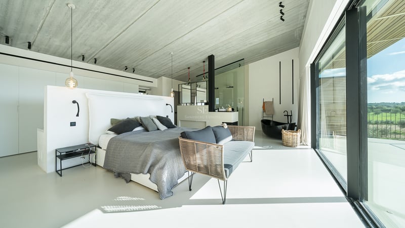 Modernt huvudsovrum med grå säng, betongtak och integrerat svart fristående badkar.