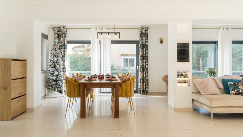Espace salle à manger moderne avec table en bois, chaises en velours jaune, sapin de Noël et grandes baies vitrées.