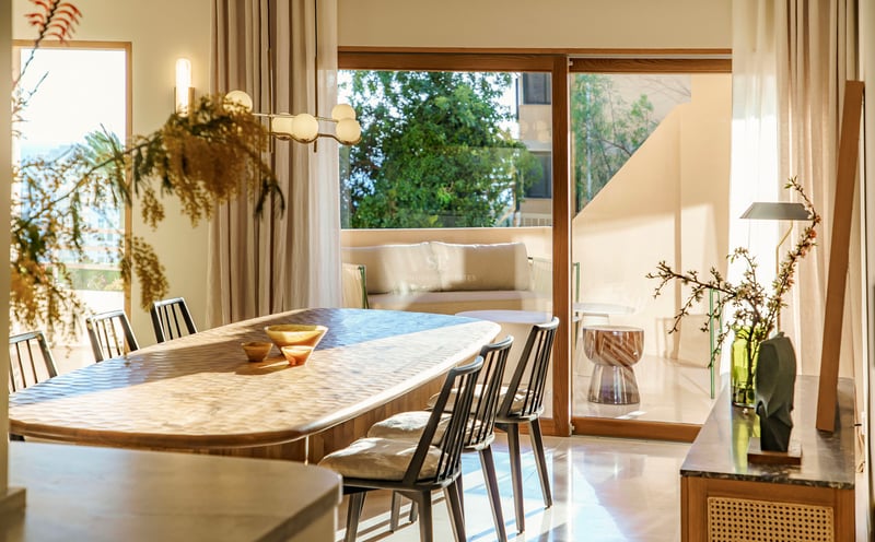 Sonnendurchflutetes Esszimmer mit handgeschnitztem Holztisch und schwarzen Stühlen vor großen Glasschiebetüren.