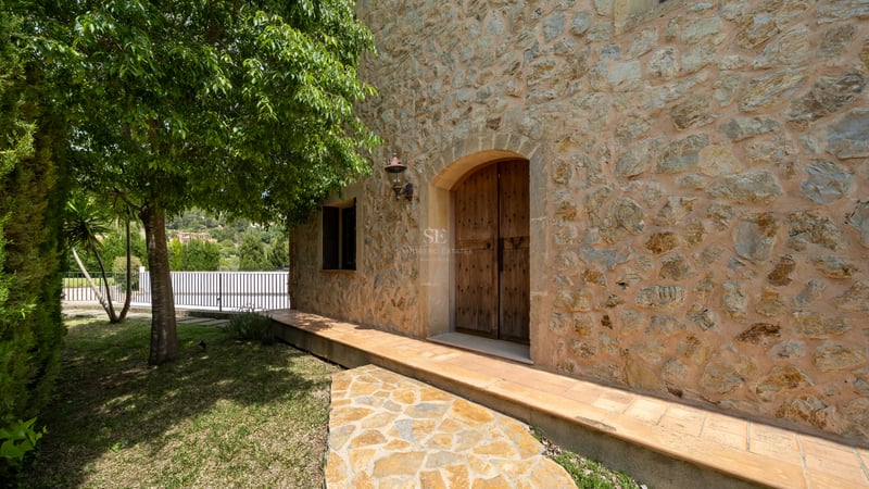 Portes doubles en bois voûtées dans une façade en pierre naturelle avec une lanterne en fer et un chemin ombragé.