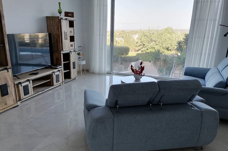 Salon moderne avec canapés en tissu gris, sol en grès poli et grande baie vitrée donnant sur la verdure.