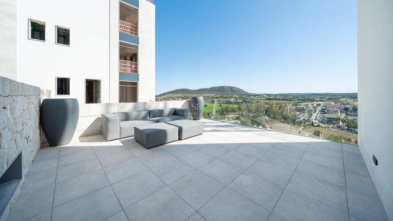 Terrasse au design épuré avec canapé gris, garde-corps en verre et vue sur le paysage naturel.