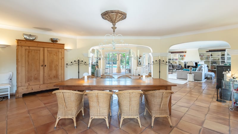 Salle à manger spacieuse avec table en bois, chaises en osier, sol en terre cuite et vues sur la piscine.
