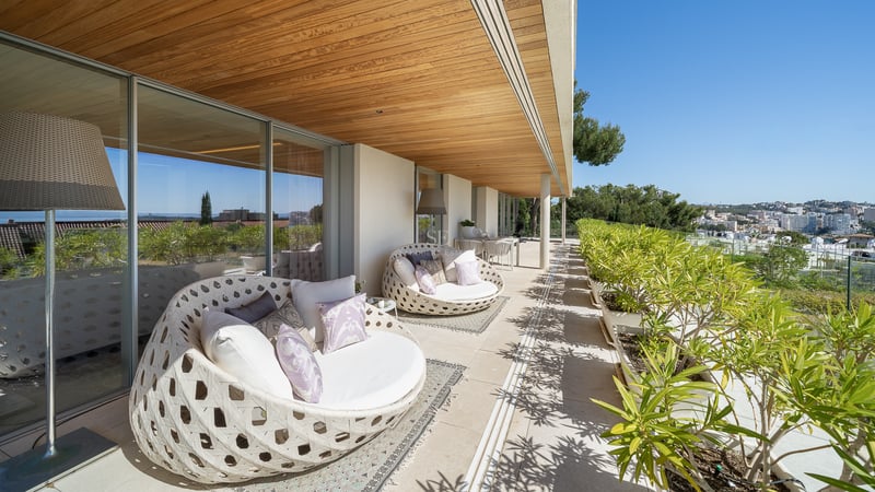 Sonnige Terrasse mit runden weißen Loungesesseln, Holzdecke und Blick auf die mediterrane Bepflanzung.