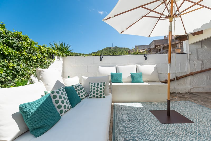 Terrasse privée en pierre blanche avec banquettes intégrées, coussins colorés, grand parasol et vue sur la montagne.
