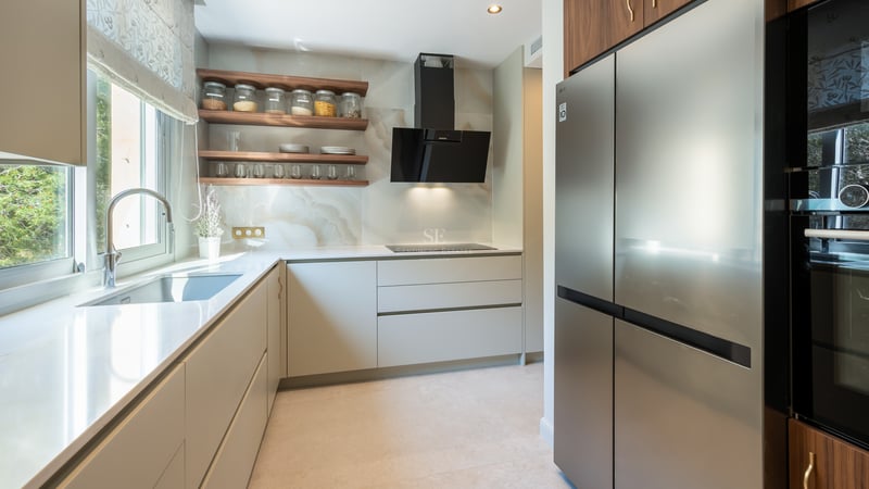 Contemporary kitchen featuring white countertops, walnut shelving, marble backsplash, and stainless steel appliances.