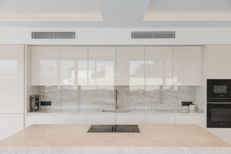 Minimalistische Küche mit cremefarbenen Glanzschränken, Marmorinsel und integrierten High-End-Geräten.