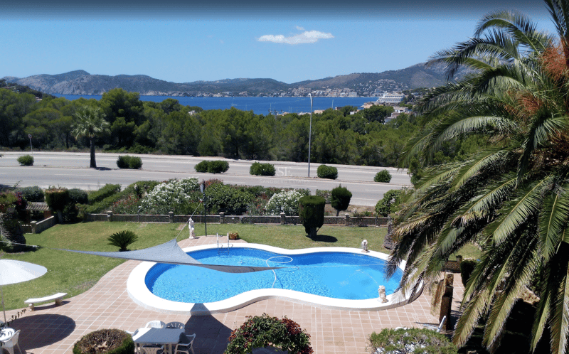 Piscina en forma de riñón rodeada de terracota y jardín con vistas al Mediterráneo y las montañas.