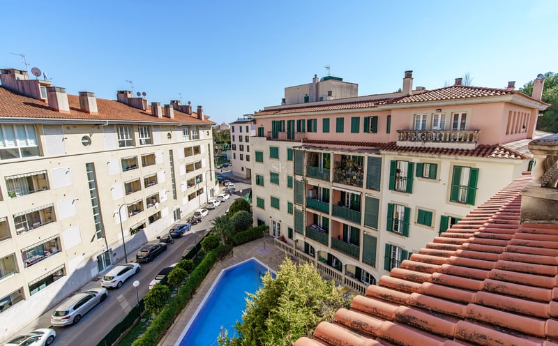 Flygvy över en blå pool omgiven av medelhavsbyggnader med gröna fönsterluckor och terrakottatak.