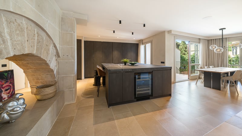 Cuisine haut de gamme avec îlot sombre, cave à vin, arche en pierre naturelle et salle à manger lumineuse.