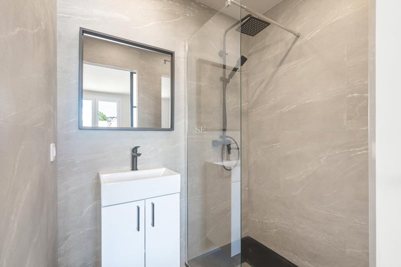 Modernes Badezimmer mit grauen Steineffekt-Fliesen, Glasduschwand, Regenduschkopf und mattschwarzen Armaturen.