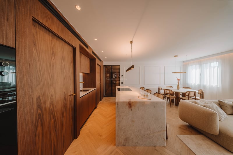 Cuisine moderne à aire ouverte avec un grand îlot en marbre, des armoires en noyer et un sol en chevrons.