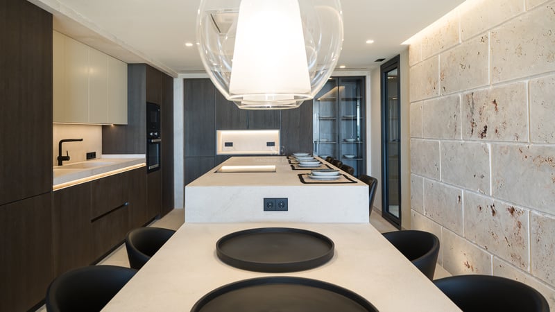 Cuisine moderne avec un grand îlot en pierre, des armoires en bois sombre et un mur en pierre naturelle texturée.