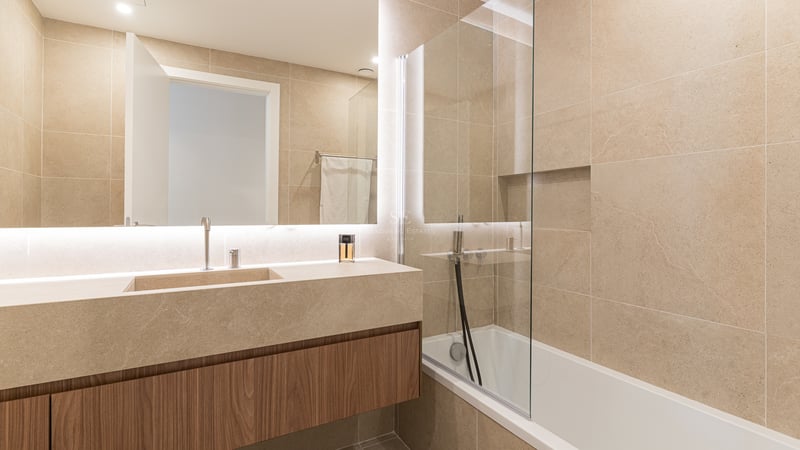 Modern bathroom featuring a floating wood vanity, large-format stone tiles, and a backlit mirror.