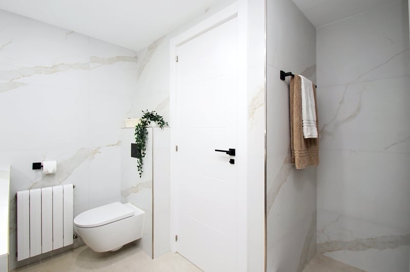 Modernt badrum med stora plattor i marmoreffekt, vägghängd toalett och detaljer i mattsvart.