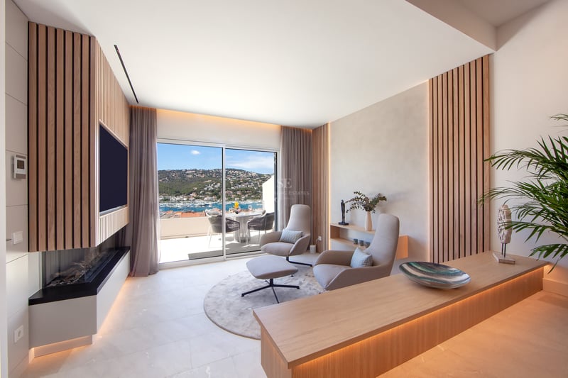 Salon moderne avec lattes de bois, fauteuils design et vue panoramique sur le port à travers des baies vitrées.