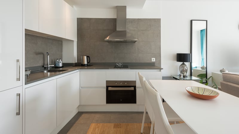 Cuisine blanche moderne avec crédence grise, appareils en inox et table à manger blanche.