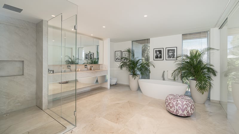 Modernes Badezimmer mit Travertinboden, Doppelwaschtisch, Glasdusche und einer weißen freistehenden Badewanne.