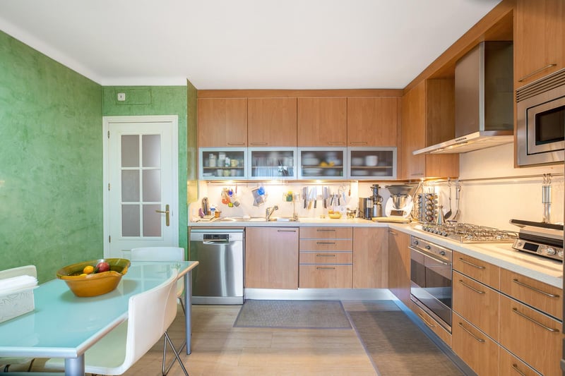 Moderne Holzküche mit Edelstahlgeräten, grüner Akzentwand und einem Glas-Esstisch.