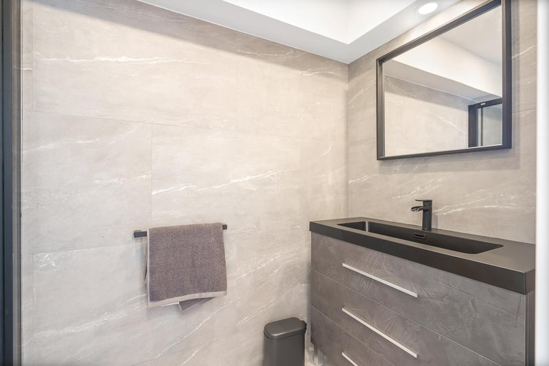 Moderner Waschtisch mit grauen Steinfliesen, schwarzem integriertem Waschbecken und schwarzem Spiegelrahmen.