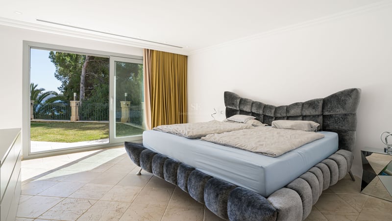 Zeitgenössisches Schlafzimmer mit grauem Samtbett und Glasschiebetüren zum mediterranen Garten.