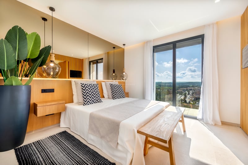 Chambre moderne avec finitions en chêne, baie vitrée toute hauteur et mur en miroir derrière le lit.