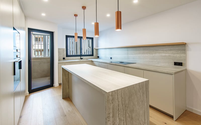 Cuisine lumineuse avec îlot en travertin, suspensions en cuivre et parquet en bois clair.