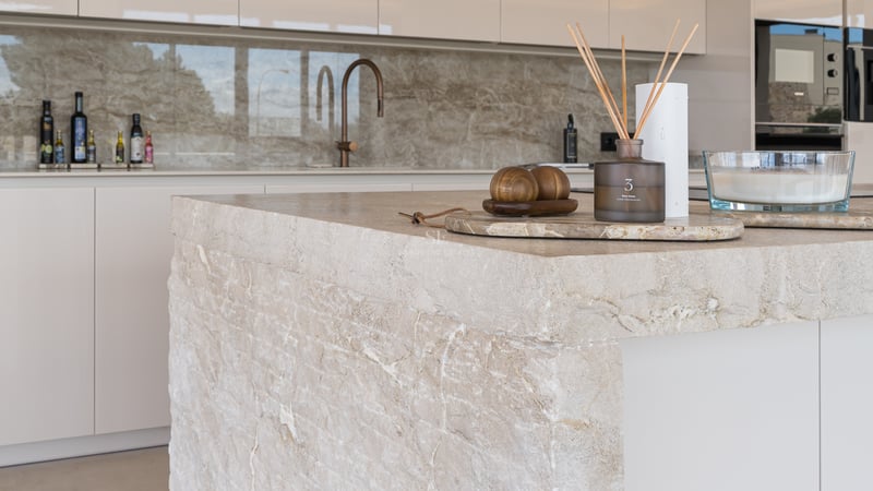 Nahaufnahme einer Kücheninsel aus Naturstein mit Kupfer-Armatur und minimalistischen Dekoelementen.