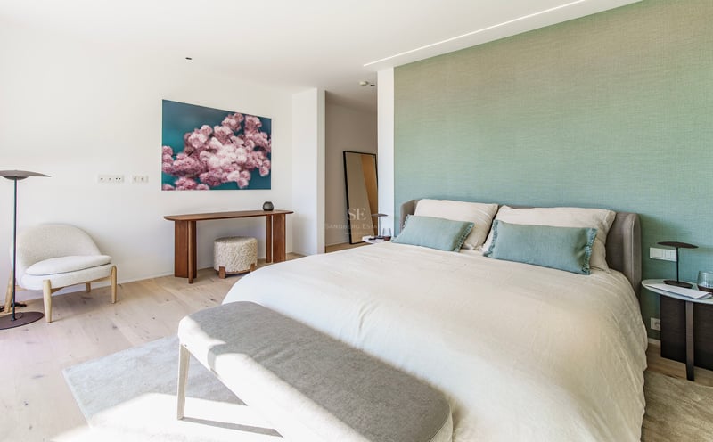 Chambre principale lumineuse avec mur vert sauge, grand lit et mobilier design sur parquet clair.