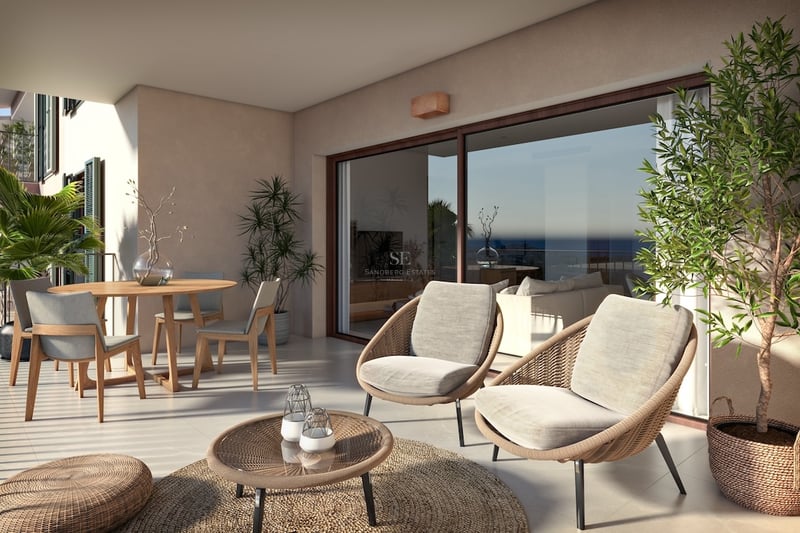 Modern terrass med rottingfåtöljer, matbord i trä och stora glasdörrar som reflekterar havet.