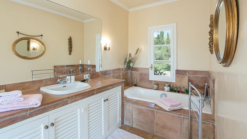 Salle de bain lumineuse avec plans en terre cuite, meubles à persiennes blanches, baignoire encastrée et miroirs.