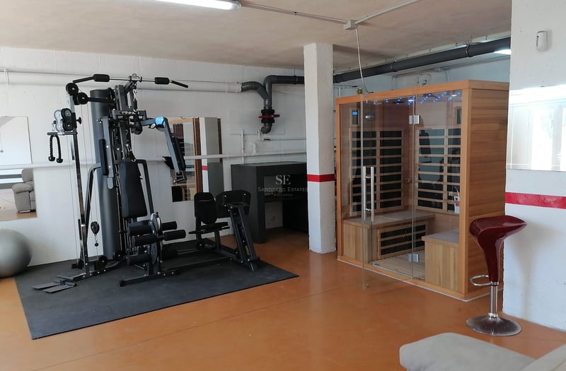 Salle de fitness intérieure avec appareil de musculation multifonction et cabine de sauna en bois.