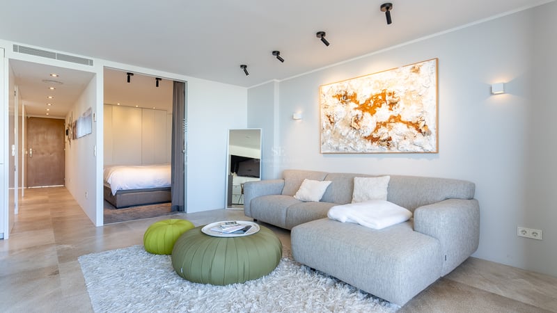 Helles Wohnzimmer mit grauem Sofa, grünen Hockern und Blick in das angrenzende Schlafzimmer.
