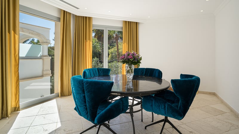 Moderner Essbereich mit rundem Marmortisch, blauen Samtstühlen und Blick durch bodentiefe Fenster.